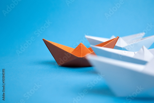 white paper boats following orange paper boat, on blue backgroung, for leadership, team and business concept.