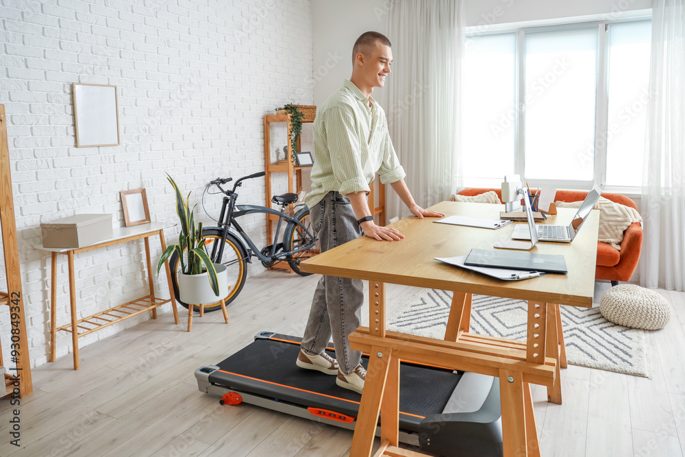 Young man video chatting on treadmill at table in office Young man video chatting on treadmill at table in office
