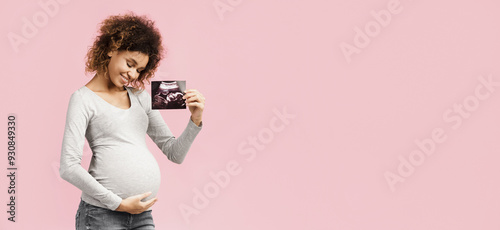 Happy afro pregnant woman with her baby sonography, enjoying first photo of her unborn child, pink background