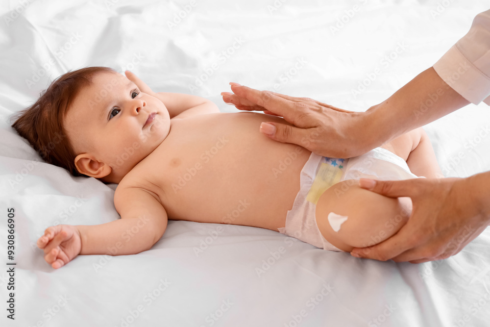 Mother applying cream on her little baby's leg in bedroom, closeup Mother applying cream on her little baby's leg in bedroom, closeup