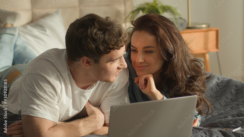 Two people couple man woman looking at laptop screen girlfriend show finger discussing talking chatting watching movie film together weekend home bedroom lying on bed relax boyfriend male female smile Two people couple man woman looking at laptop screen girlfriend show finger discussing talking chatting watching movie film together weekend home bedroom lying on bed relax boyfriend male female smile