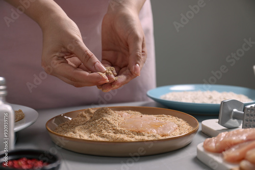 Making schnitzel. Woman coating slice of meat with bread crumbs at grey table, closeup