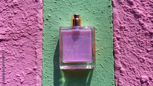 A square perfume bottle in a soft blush pink, with a satin-like finish, placed in front of a pink cement concrete wall. The gentle color palette and the wallâ€™s texture offer a delicate, minimalist photo