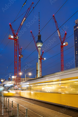 The famous Television Tower of Berlin at night with red construction cranes and a motion blurred tramway