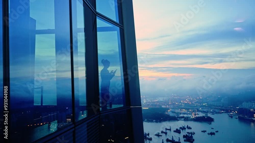 Mid adult businesswoman standing in a corporate windows with view of the city, talking on her mobile phone