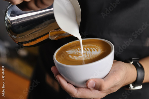 Pouring milk into a cup of coffee in hand and making latte art, photography