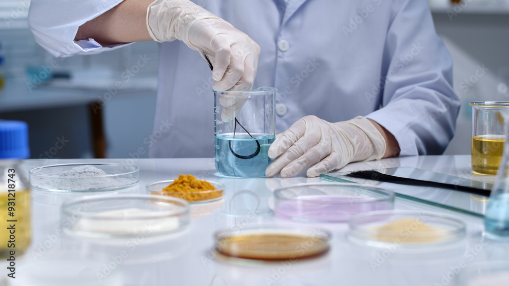 The scientist is dipping a sample of black hair into a blue solution. Scenes of scientific experiments and hair research. Laboratory setting, chemicals are stored in many petri dishes The scientist is dipping a sample of black hair into a blue solution. Scenes of scientific experiments and hair research. Laboratory setting, chemicals are stored in many petri dishes
