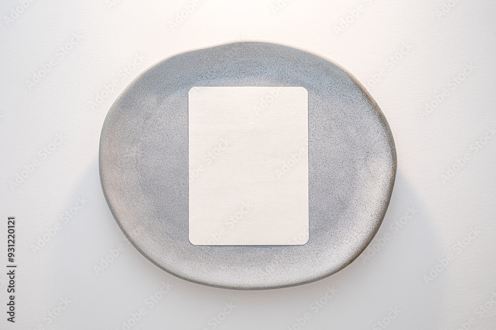 Blank paper placed on smooth gray plate for menu, note, recipes styled in minimalistic dining setting.