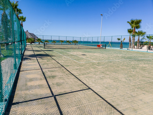 A tennis court with very poorly maintained synthetic grass and also with the sea in the background and lighting