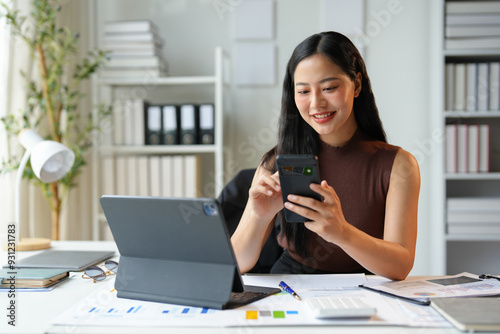 Happy Asian businesswoman in office while using smartphone to contact customer, online video call on documents, business finance, marketing, company taxes. Online business contact.