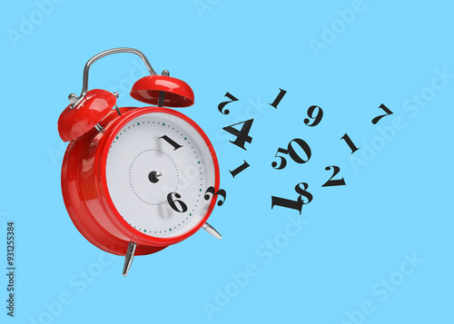 Numbers flying away from alarm clock on light blue background. Time related concepts photo