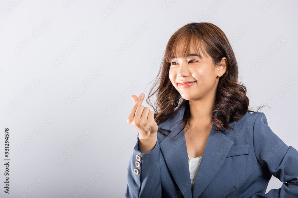 Confident business woman stands with a smile, creating a mini heart sign with her finger on a white background. Asian portrait of a beautiful young female sending love for Valentine's Day, studio shot Confident business woman stands with a smile, creating a mini heart sign with her finger on a white background. Asian portrait of a beautiful young female sending love for Valentine's Day, studio shot