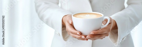 A person in a white outfit holding a cup of coffee with both hands, symbolizing warmth, comfort photo