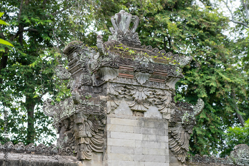 Ornately carved Balinese wall tower. Moss, hand carved reliefs, trees growing from cracks in stone.