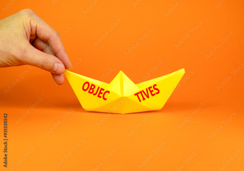 Fototapeta premium Objectives symbol. Concept word Objectives on beautiful yellow paper boat. Beautiful orange background. Businessman hand. Business objectives concept. Copy space.