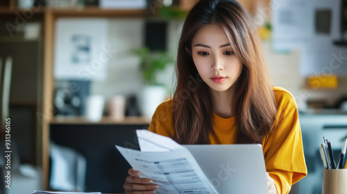 Young Asian woman planning her monthly finances, using a laptop to manage deductions