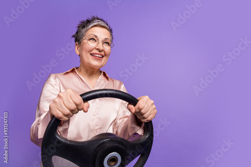 Photo portrait of attractive retired woman driving steering wheel dressed stylish satin clothes isolated on violet color background