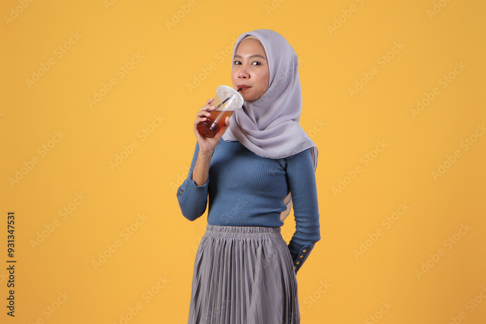 portrait of happy asian indonesian muslim woman drinking cold ice tea in plastic cup on isolated yellow background portrait of happy asian indonesian muslim woman drinking cold ice tea in plastic cup on isolated yellow background