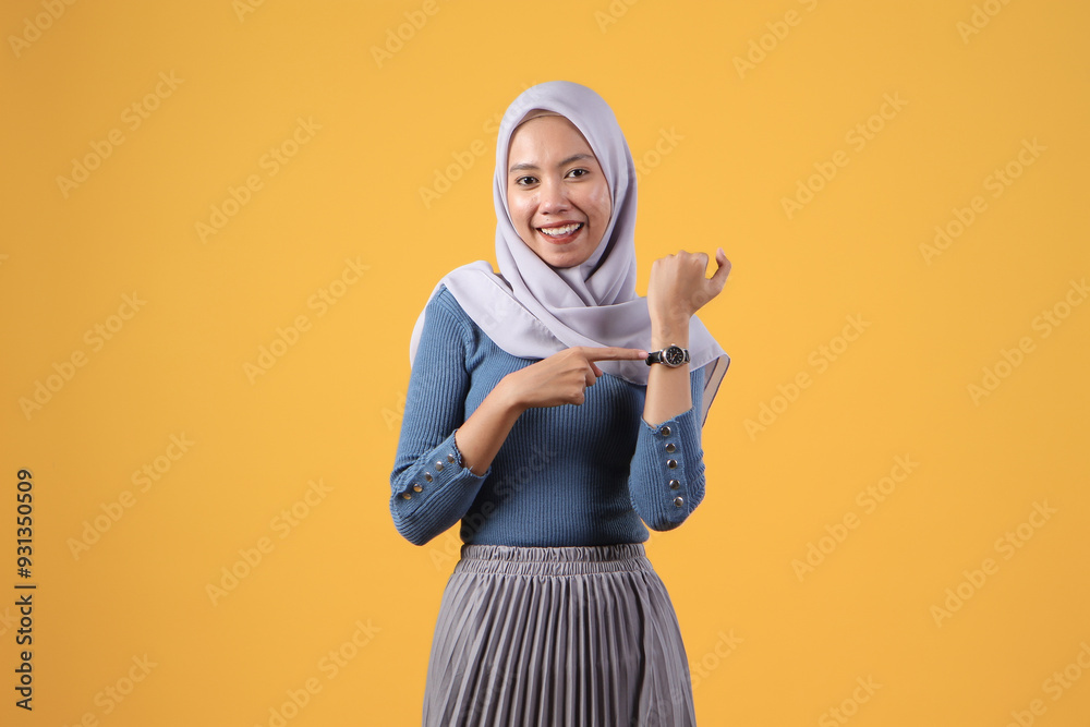 happy asian indonesian muslim woman using wrist watch on isolated yellow background happy asian indonesian muslim woman using wrist watch on isolated yellow background