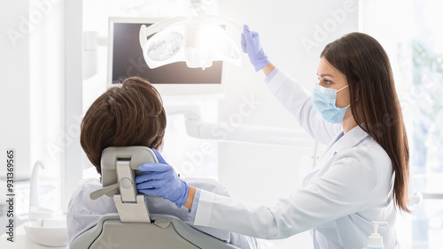 Dentist female doctor in mask turning on lamp before treating patient