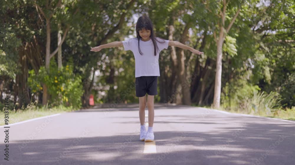 A cute little girl is playing balance on a line in a park. She spreads her arms out and walks carefully so as not to stray from the line, with different poses, looking happy and joyful while playing. A cute little girl is playing balance on a line in a park. She spreads her arms out and walks carefully so as not to stray from the line, with different poses, looking happy and joyful while playing.
