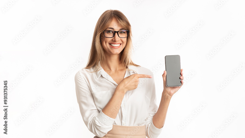 Mobile App. Smiling Woman Pointing Finger At Smartphone Blank Screen Standing On White Studio Background. Isolated, Mockup Mobile App. Smiling Woman Pointing Finger At Smartphone Blank Screen Standing On White Studio Background. Isolated, Mockup