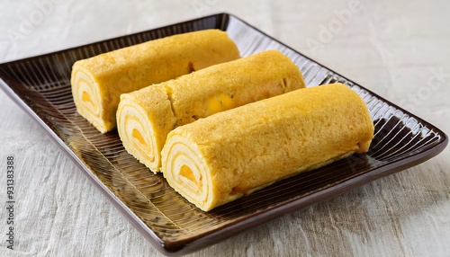 Three Delicious Japanese Tamagoyaki Egg Rolls on a Brown Plate photo