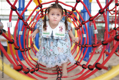 A little girl is walking through a red and blue rope tunnel. She is wearing a blue dress with a white collar photo