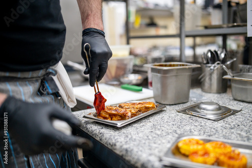 Canvas Print A chef in a professional kitchen is glazing cooked meat with sauce, focusing on the action of brushing the sauce