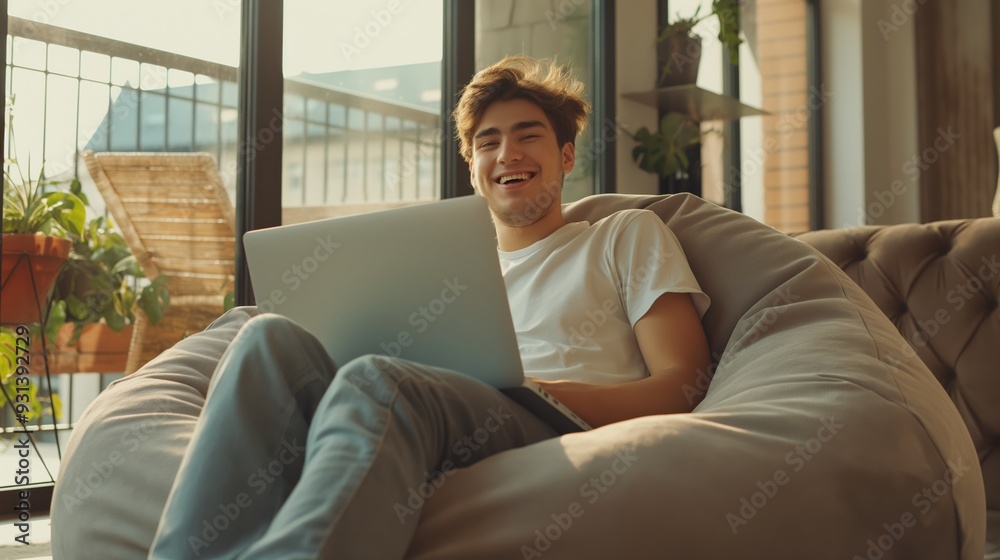 Full-Length View of Happy Young Man Sitting in Bean Bag Chair Unboxing New Laptop Full-Length View of Happy Young Man Sitting in Bean Bag Chair Unboxing New Laptop