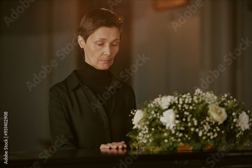 Senior mourning widow touching black coffin as goodbye gesture