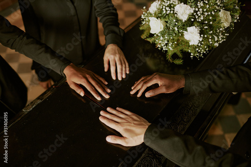 High angle shot of unrecognizable biracial hands on coffin next to bouquet of white roses photo