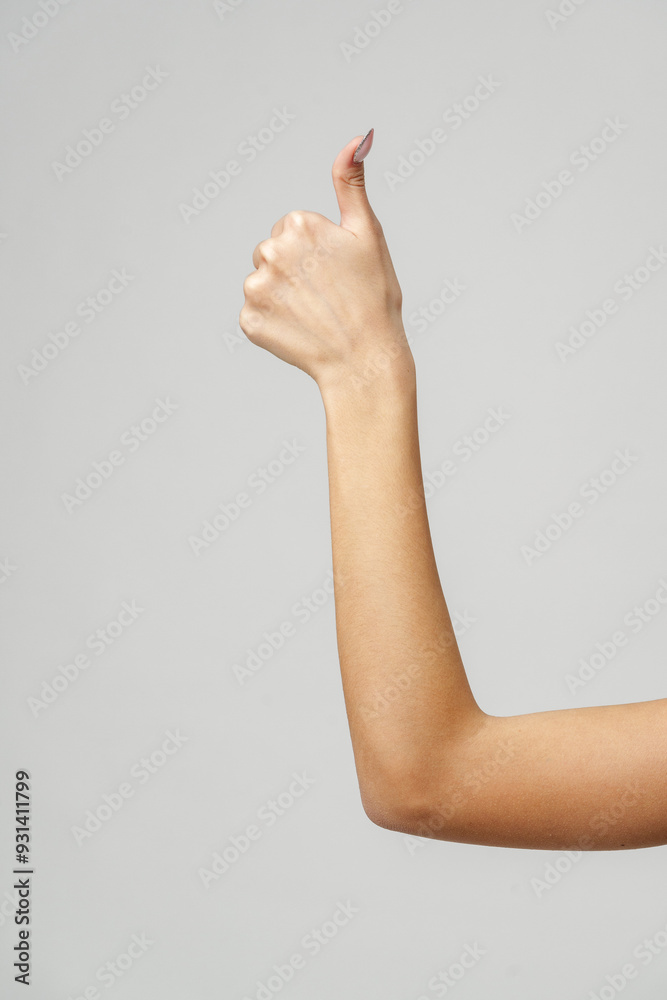 Woman's Arm Showing Thumbs Up Gesture Against Gray Background Woman's Arm Showing Thumbs Up Gesture Against Gray Background