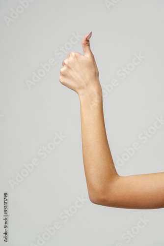 Woman's Arm Showing Thumbs Up Gesture Against Gray Background