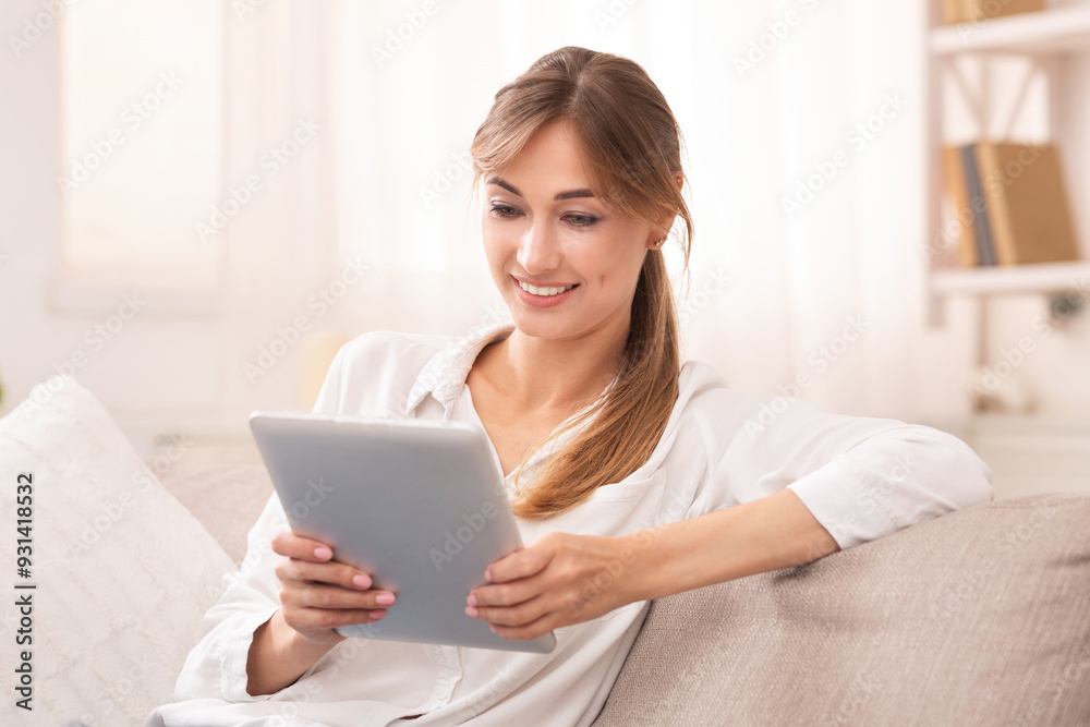 Smiling Young Woman Using Digital Tablet Relaxing On Sofa At Home. Selective Focus Smiling Young Woman Using Digital Tablet Relaxing On Sofa At Home. Selective Focus