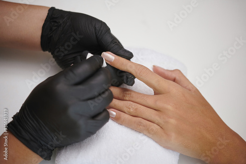 Hands wearing black gloves giving manicure treatment to someones hands on a white towel creating a sense of care photo