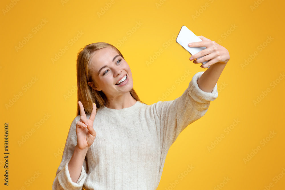 Smiling teenage girl taking selfie on smartphone, showing peace gesture, orange studio background with copy space Smiling teenage girl taking selfie on smartphone, showing peace gesture, orange studio background with copy space