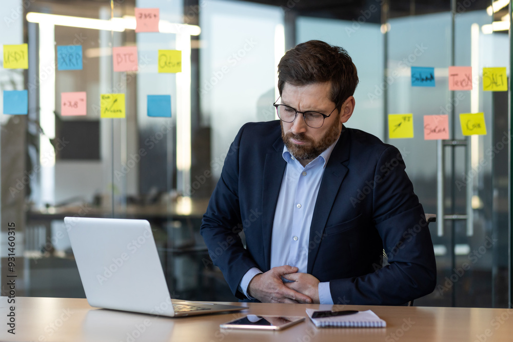 Business professional suffers from stomach pain while working at desk. Man in formal attire shows signs of stress and discomfort, affecting productivity. Work environment impacts health efficiency. Business professional suffers from stomach pain while working at desk. Man in formal attire shows signs of stress and discomfort, affecting productivity. Work environment impacts health efficiency.