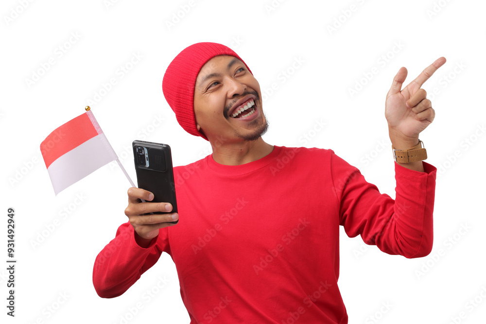 Indonesian man in a red long sleeve shirt points at empty copy space while holding the Indonesian flag and phone during Indonesia Independence Day Celebration on August 17 isolated on white background Indonesian man in a red long sleeve shirt points at empty copy space while holding the Indonesian flag and phone during Indonesia Independence Day Celebration on August 17 isolated on white background