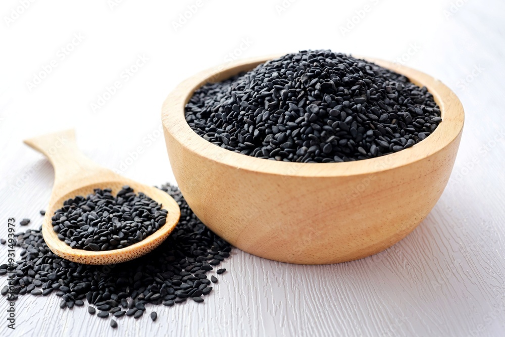 Black Sesame Seeds in a wooden bowl with a wooden spoon on white background Black Sesame Seeds in a wooden bowl with a wooden spoon on white background
