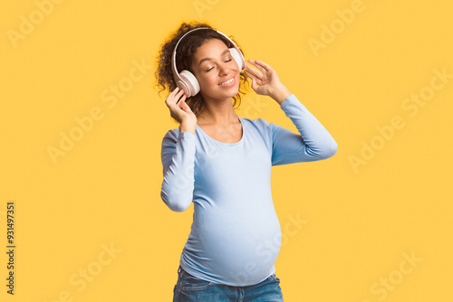 Pregnancy playlist. Afro expectant lady enjoying music in headphones, white background