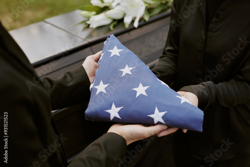 Unrecognizable hands holding American flag next to coffin photo