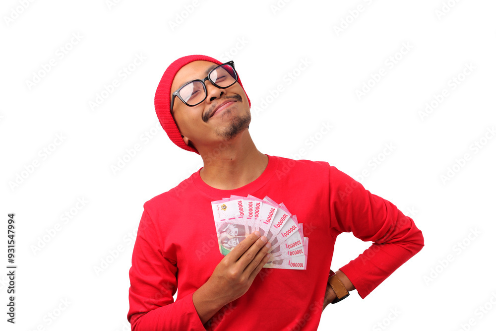 Excited Indonesian man in a red long sleeve and beanie shirt holding Indonesian Rupiah money, celebrating bonus received during Indonesia's Independence Day on August 17, isolated on white background Excited Indonesian man in a red long sleeve and beanie shirt holding Indonesian Rupiah money, celebrating bonus received during Indonesia's Independence Day on August 17, isolated on white background