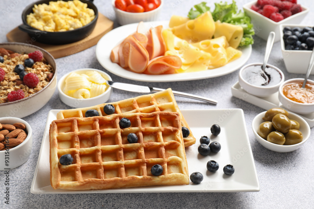 Tasty breakfast. Belgian waffles, blueberries and other food on grey textured table, closeup Tasty breakfast. Belgian waffles, blueberries and other food on grey textured table, closeup