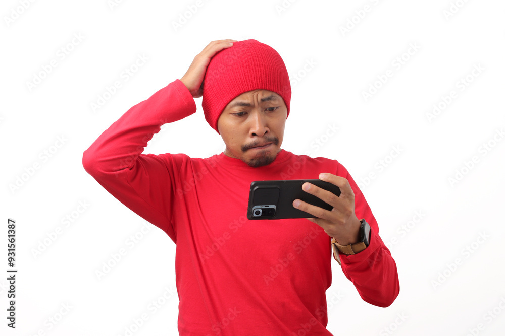 Indonesian supporter man wearing red long sleeve T-Shirt and headphone reacts to his national team's match on his phone, losing the game during injury time, Isolated on a white background Indonesian supporter man wearing red long sleeve T-Shirt and headphone reacts to his national team's match on his phone, losing the game during injury time, Isolated on a white background