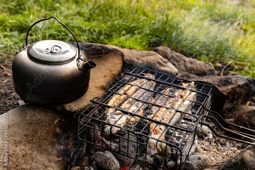 Cooking fish over an open fire at a campsite in summer.