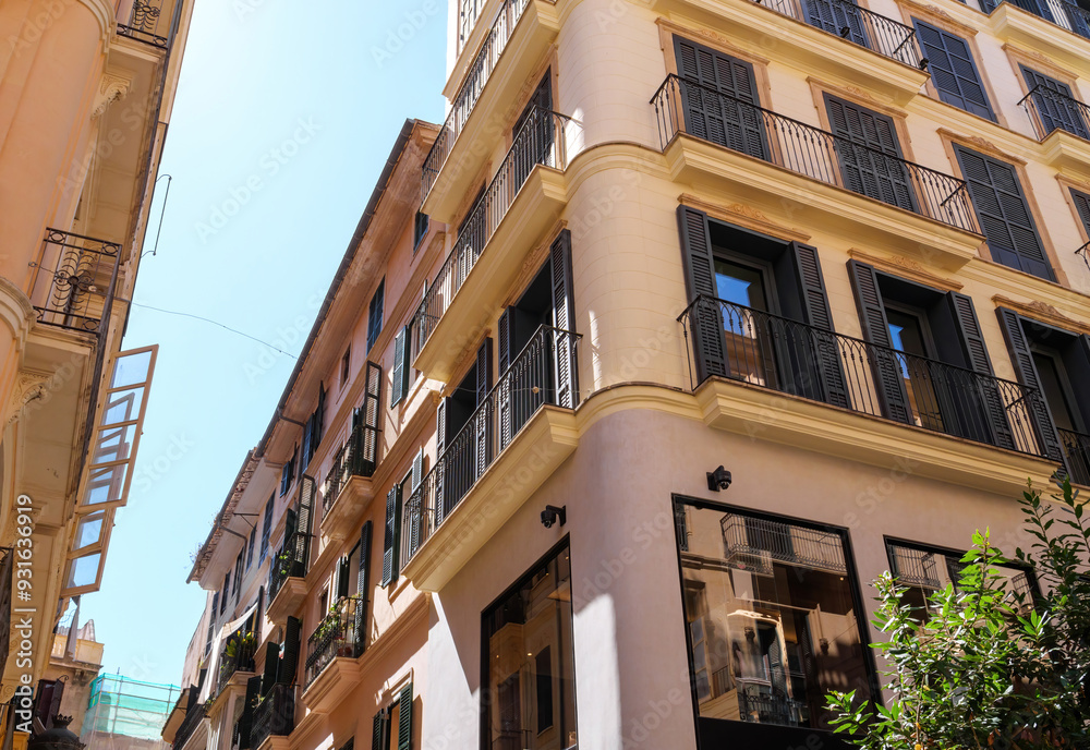 Fototapeta premium A warm day in Palma de Mallorca, featuring a luxury real estate apartment building in the center covered with sunblinds, reflecting an ideal investment property in a desirable Mediterranean location