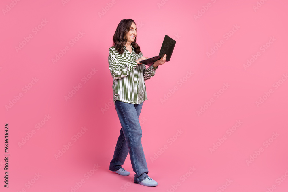 Full body portrait of pretty aged lady walk use laptop wear shirt isolated on pink color background Full body portrait of pretty aged lady walk use laptop wear shirt isolated on pink color background