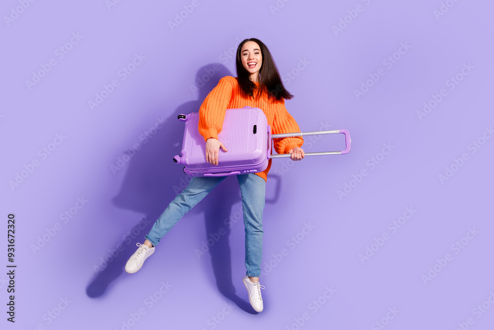 Photo of glad cheerful cute girl wear stylish orange clothes hold valise isolated on violet color background Photo of glad cheerful cute girl wear stylish orange clothes hold valise isolated on violet color background
