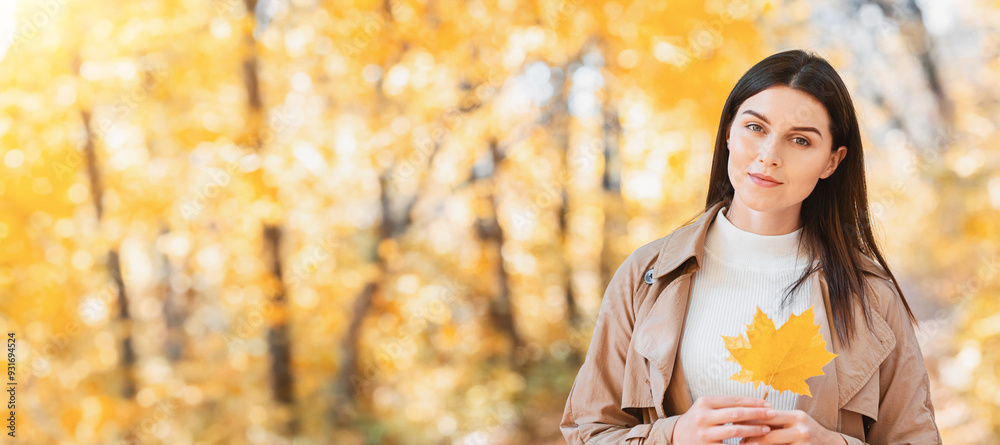 Portrait of pretty woman with yellow marple leaf posing in autumn forest, copy space